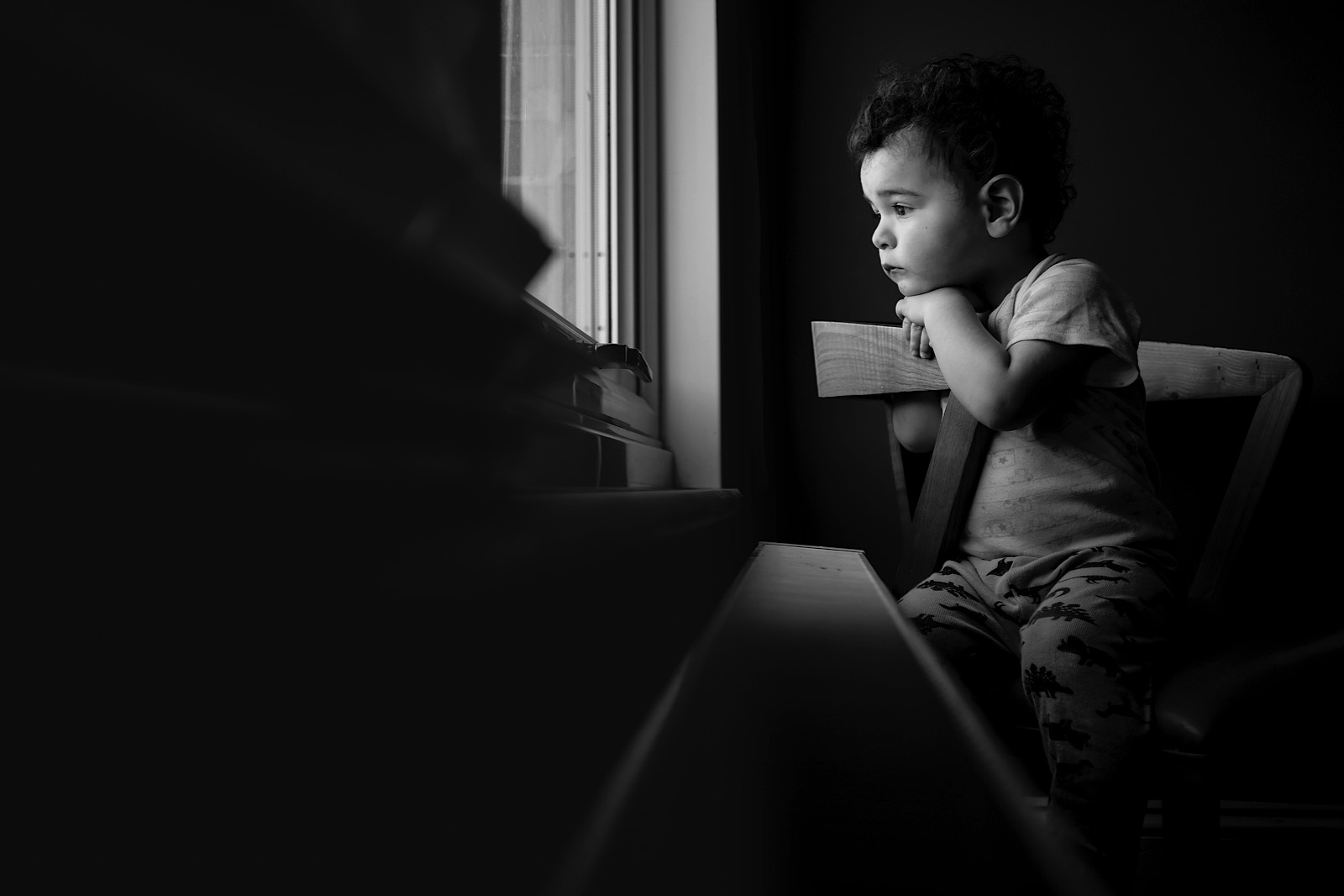 black & White image of Young boy sat on chair looking out of window