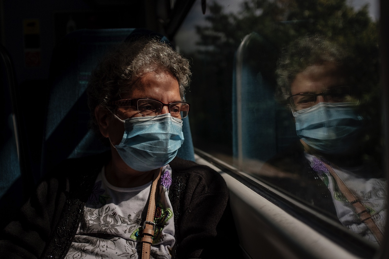 Older woman looking out of a window wearing facemask during covid