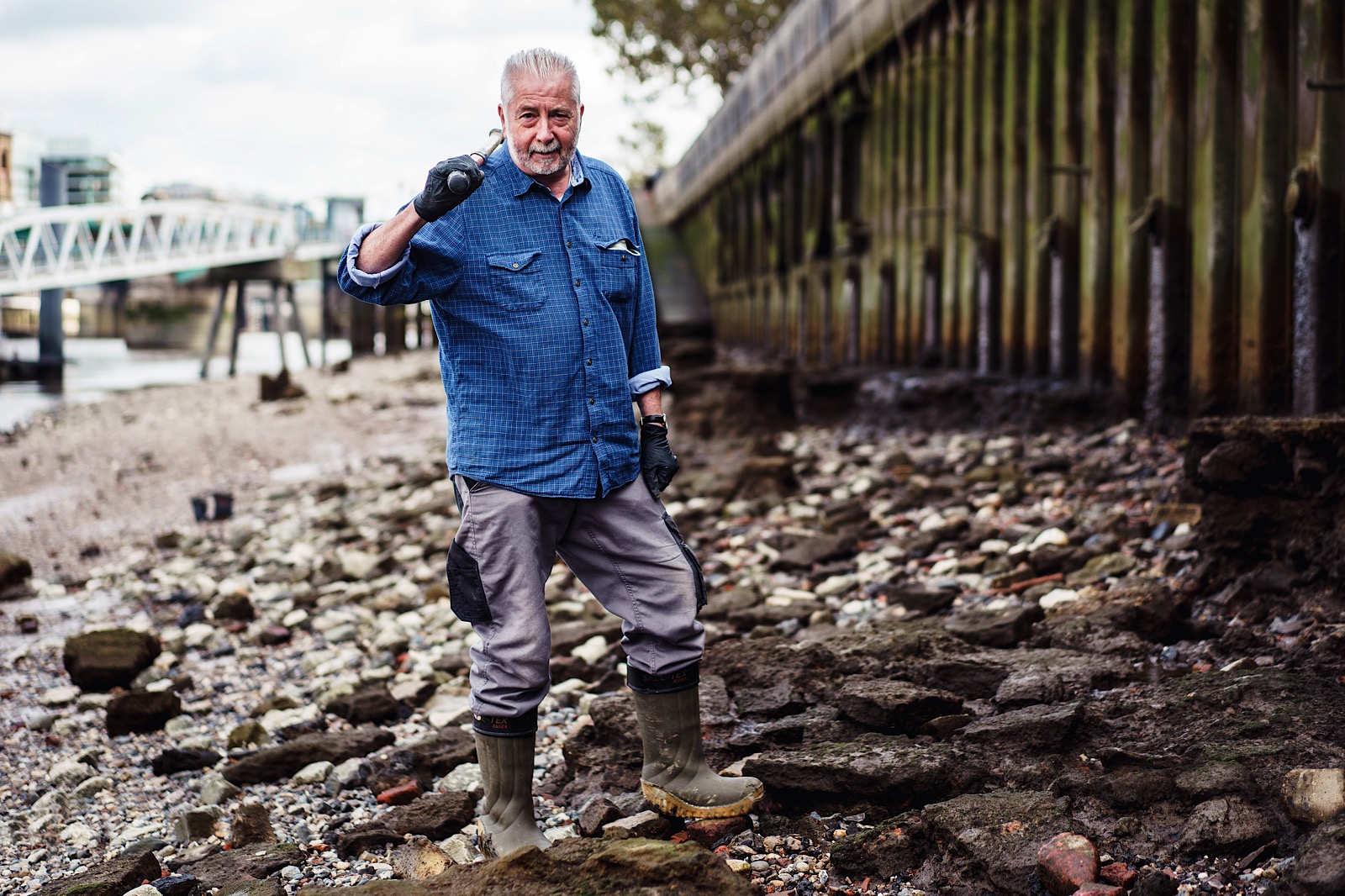 Mudlarket stood on Banks of River Thames with tool over shoulder