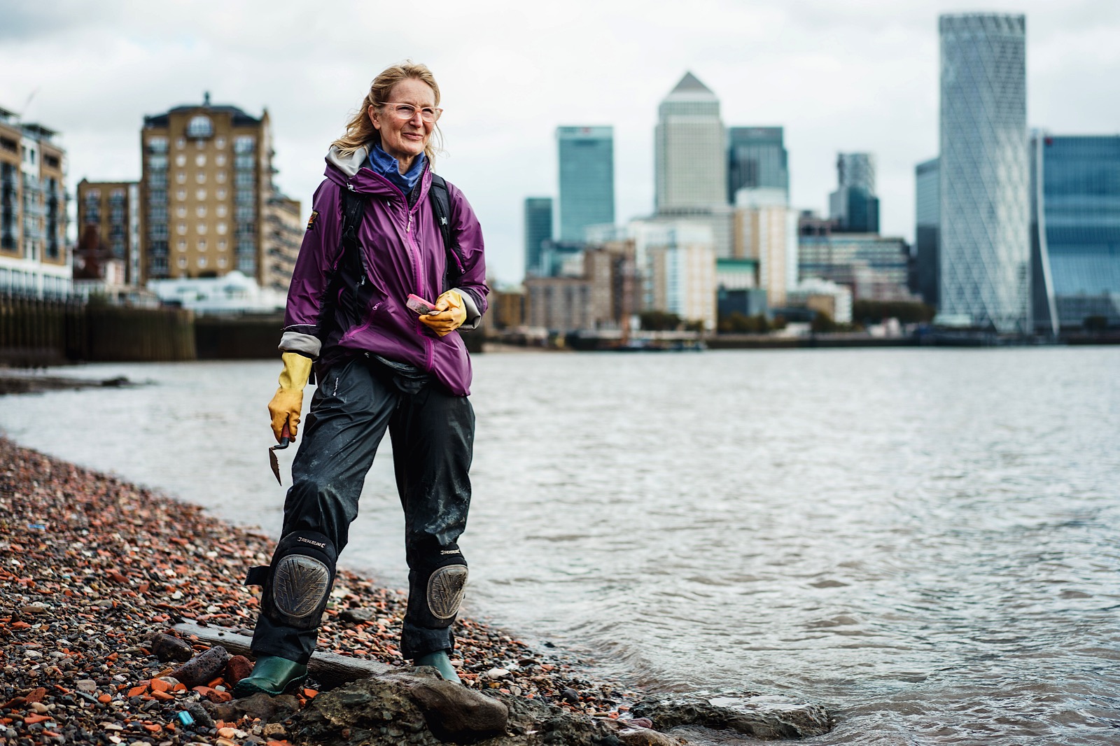 Mudlarker on shore of River Thames with trowel in her hand