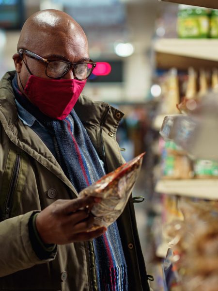 Man wearing red mask choosing crisps in supermarket