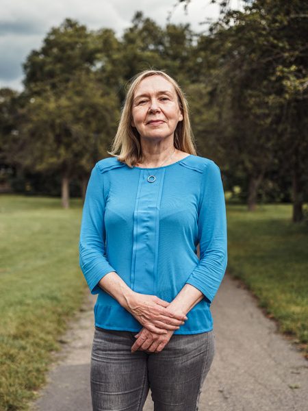 Portrait of woman stood in a park wearing blue top and jeans looking directly into camera
