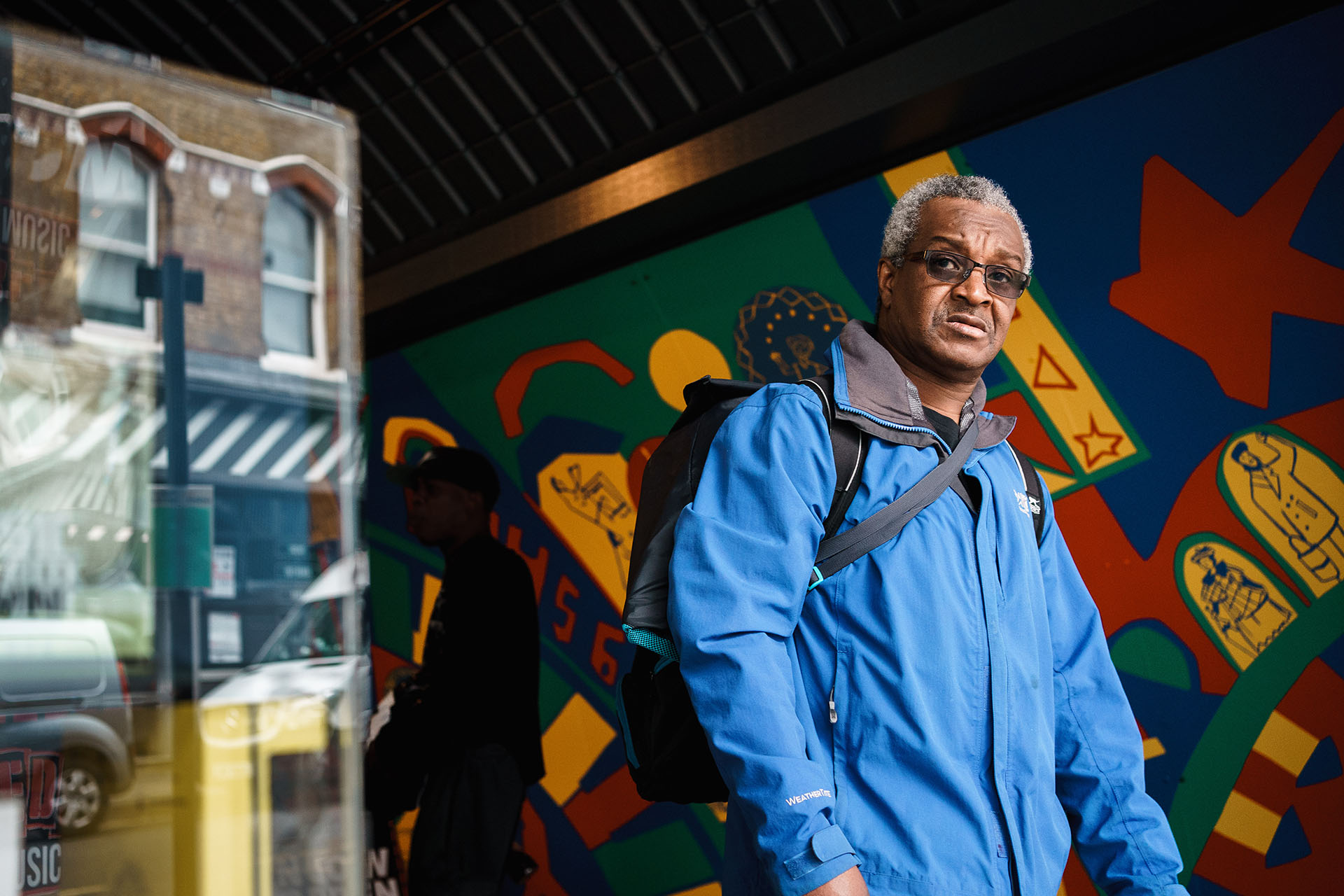 Man wearing a blue jacket walking past bright and colourful street art in Brixton