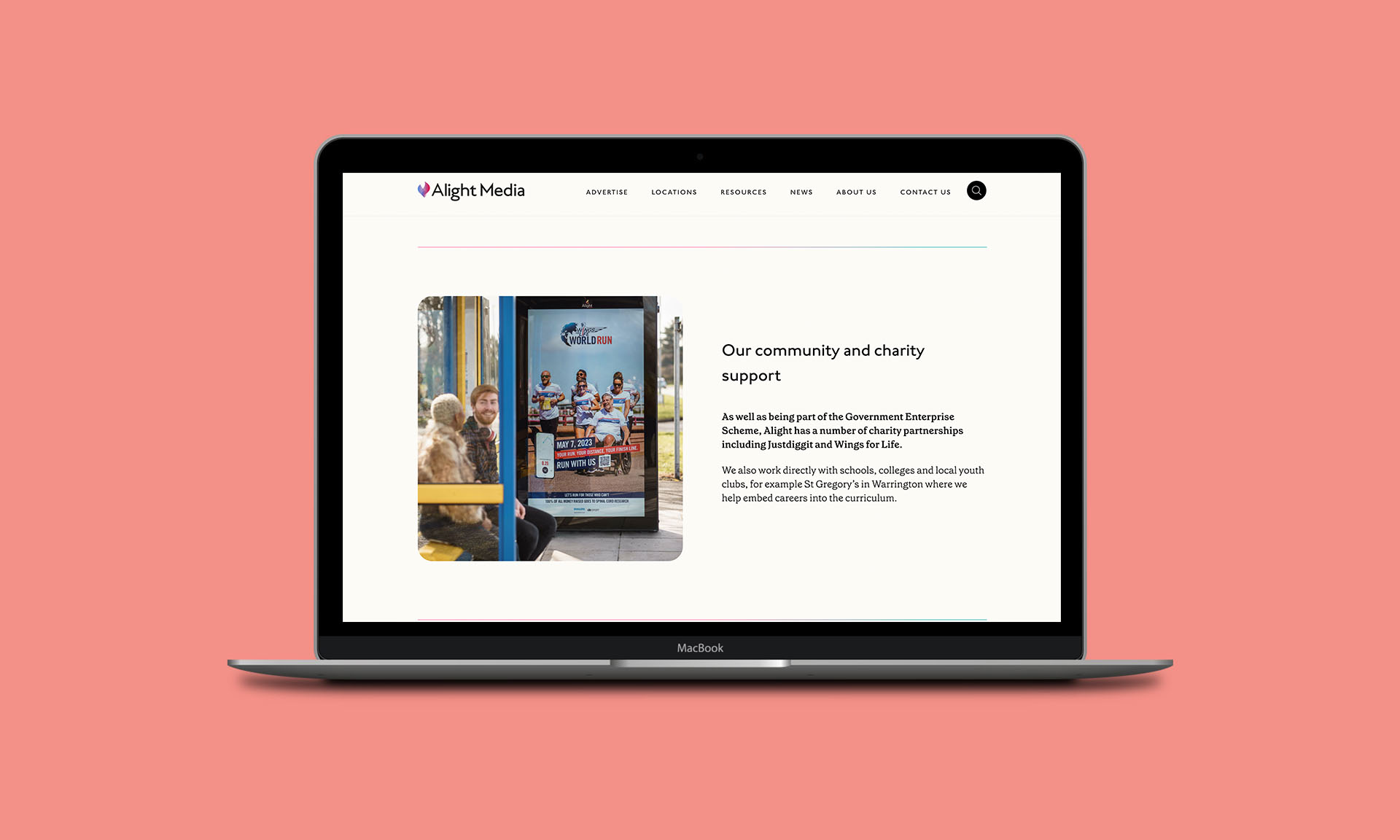 A laptop displaying the Alight Media website on a pink background, showing a community support page with an image of people at a bus stop.