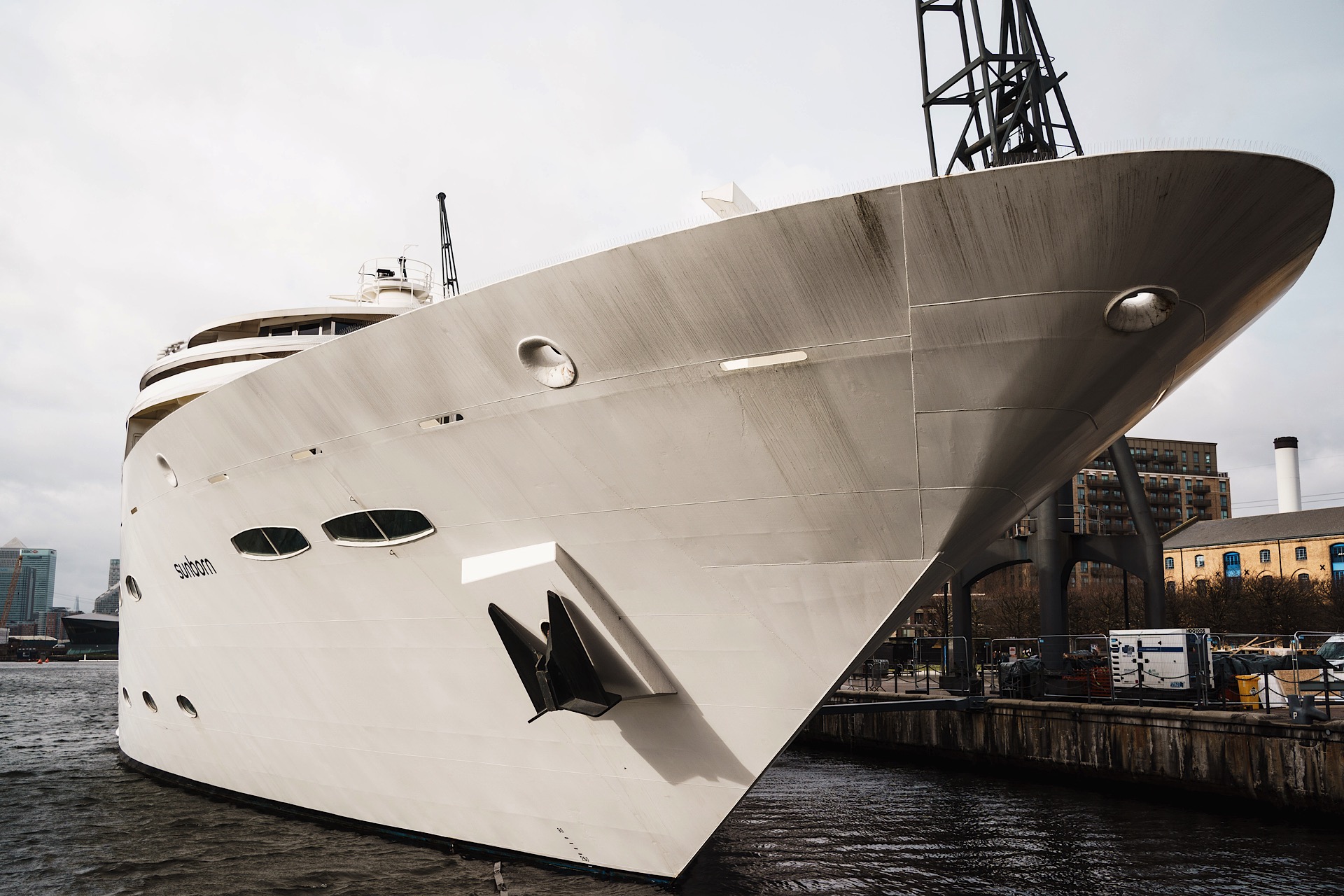 Large white yacht docked at an urban pier with buildings in the background.